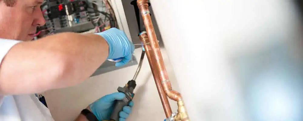 Water heater repair technician testing copper pipe connections and controls in Detroit, MI